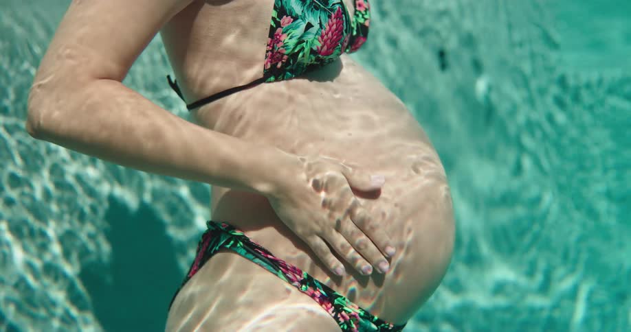 Pregnant woman in bikini strokes her belly in the swimming pool
