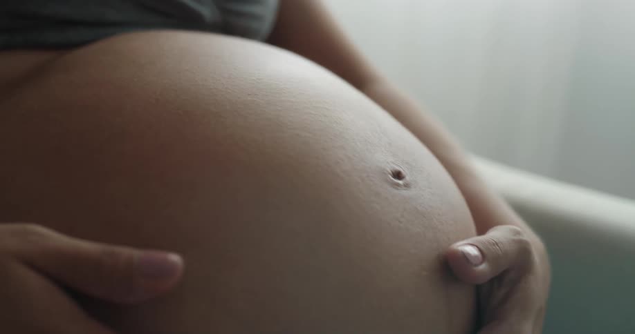 Pregnant woman strokes her belly sitting in armchair
