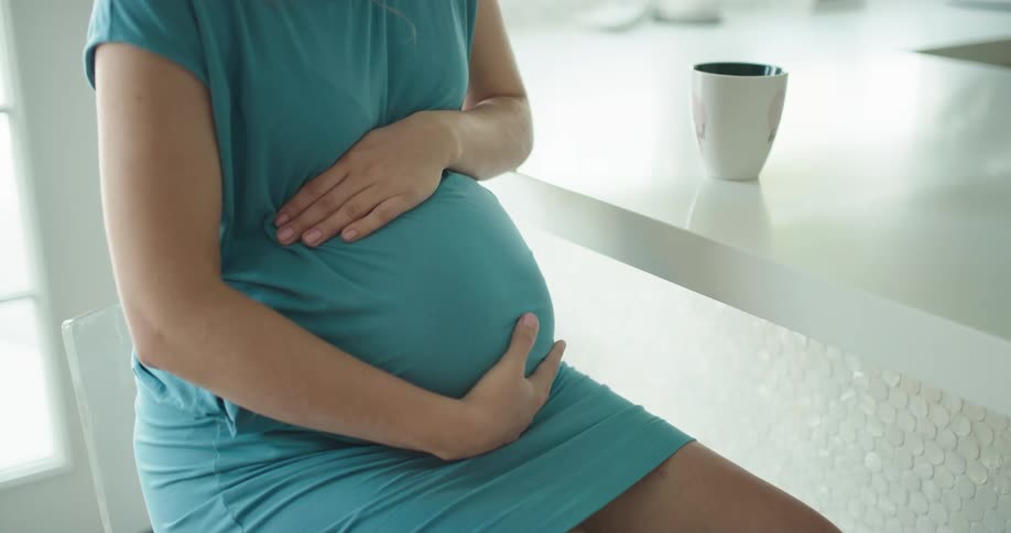Pregnant woman sitting down as she rubs her belly