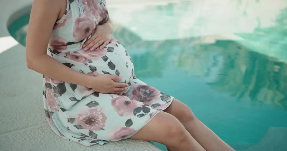 Pregnant woman wearing a dress sitting at the side of a pool