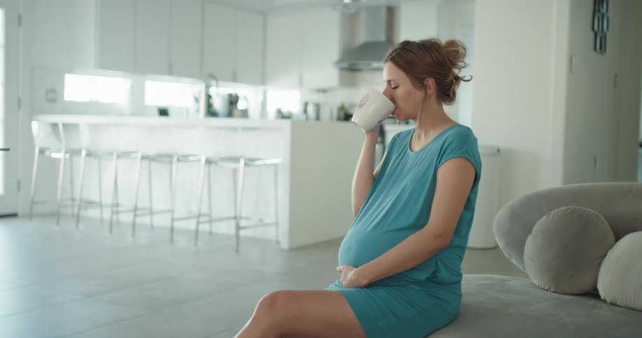 Young pregnant woman is sitting down and drinking coffee