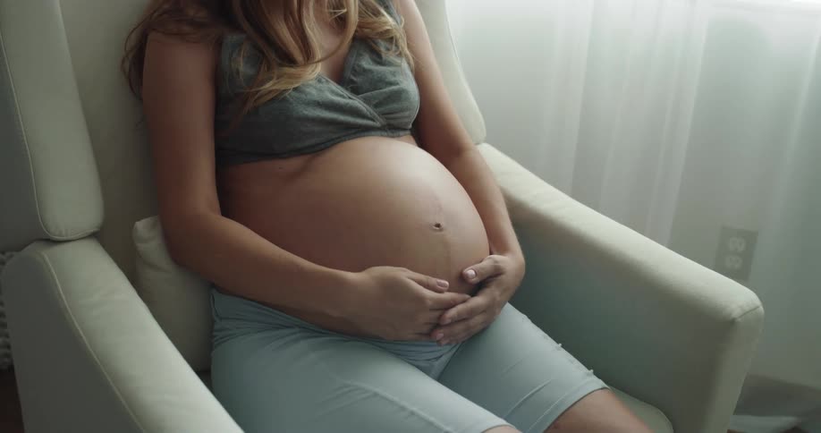 A pregnant woman rubs her belly in the chair