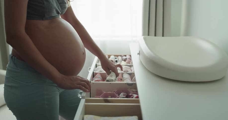 A pregnant women arranges baby clothing in a dresser
