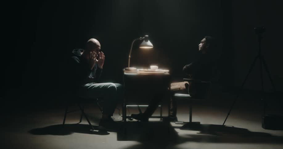 Nervous suspect talks to a detective on a dimly lit interrogation room