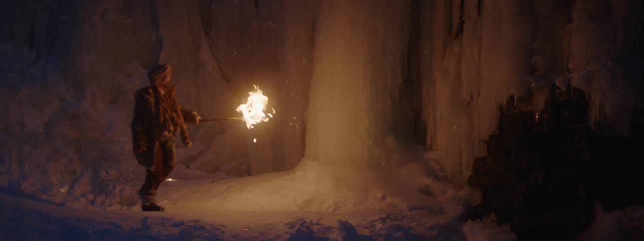 Man wearing thick fur clothes explores a dark cave with a torch