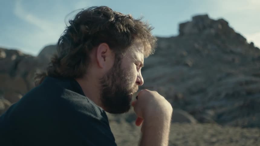 A man is outside smoking as sun shines on his face and there is a mountain in the distance