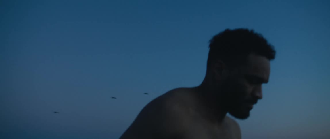 Shirtless man runs on the beach at dusk