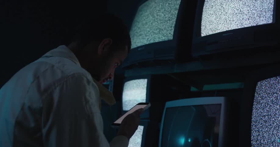 Man focuses on smartphone as several nearby televisions show signal noise