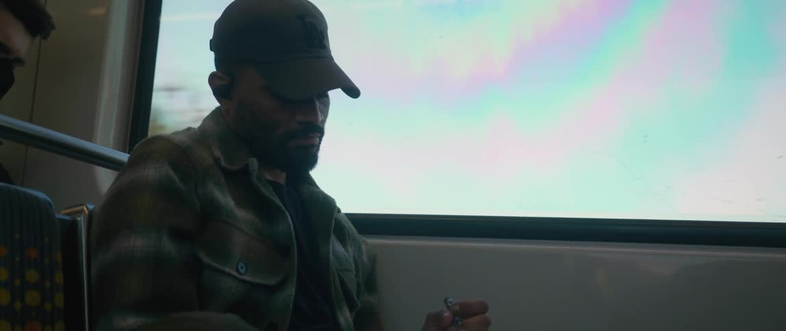 A man sits on a bus and writes in a notebook after looking out the window