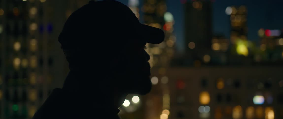 A man looks out over the buildings of a metropolis at night