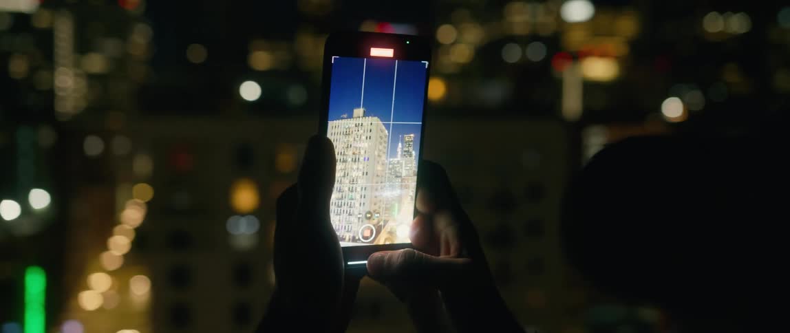 A person uses a smartphone to film buildings in a metropolis at night