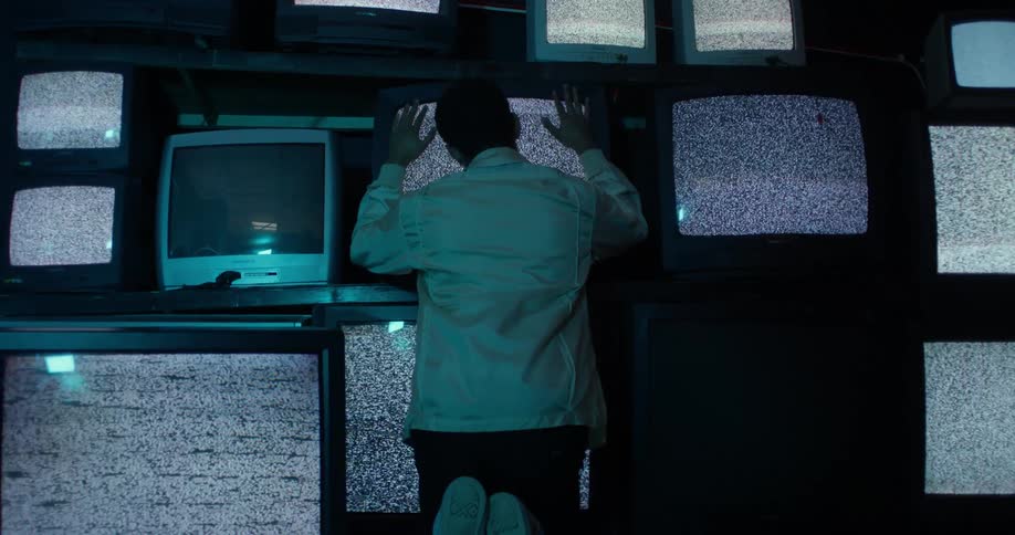 Man kneels with hishands and face pressed to on in a number of televisions showing signal noise