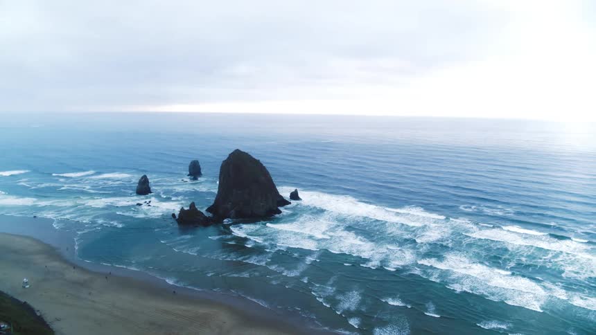 A rock formation protrudes from cannon beach with waves crashing into shore