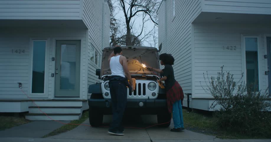 A man and a woman are looking under the hood of a car