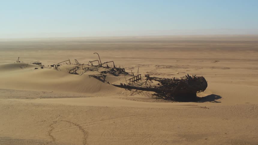 Wreckage of a large ship partially buried in sand in a desert during the day