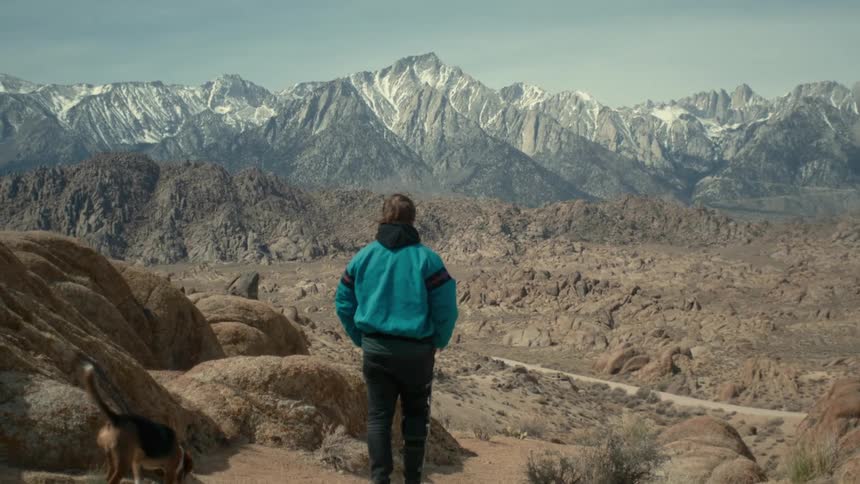 Young man and dog are outside walking in the desert