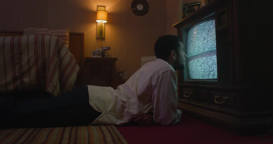 Young man is laying down on floor and watching television