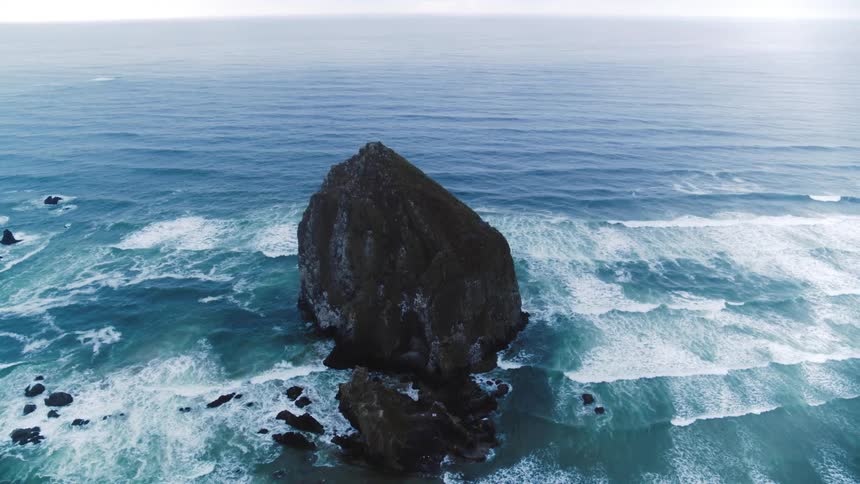 Aerial view of Pacific Ocean crashing against a massive jutting rock off cannon beach