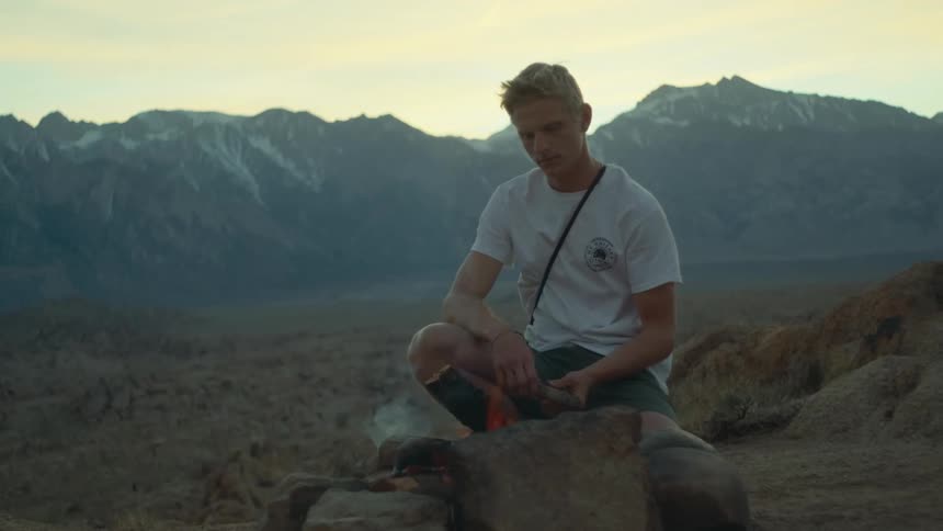 A man is sitting by a bonfire outdoors in the wilderness
