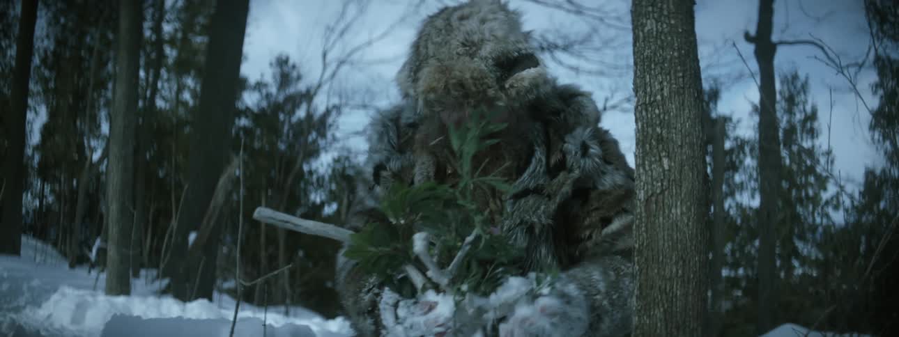 Man wearing fur winter clothes kneels on the snow on a forest and screams