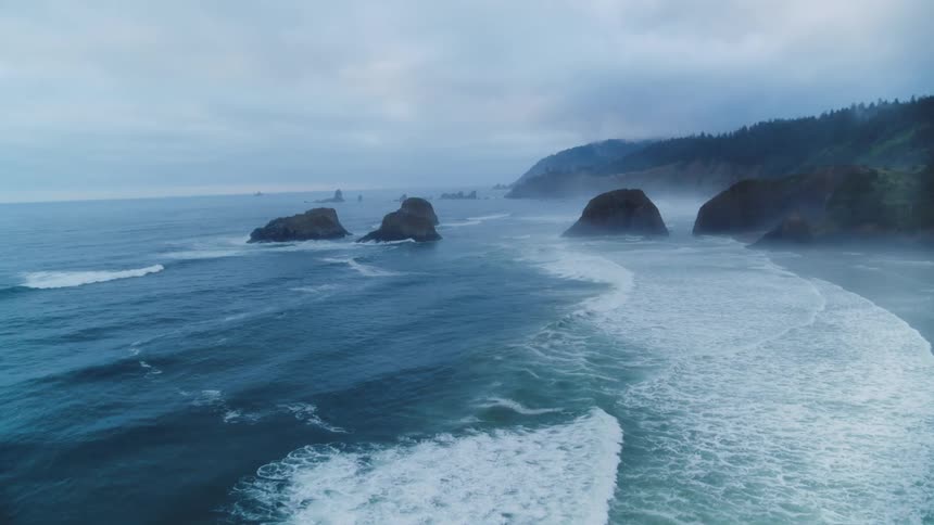 Aerial scene of waves crashing against Cannon Beach coast in Pacific Northwest with rock formations