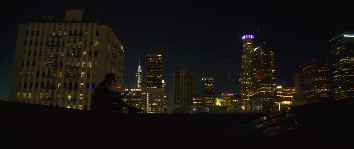 A man sits and reads on a rooftop overlooking downtown