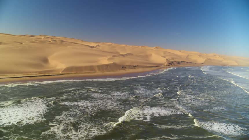 Waves crashing along the Namibian coastline with sand dunes in the background