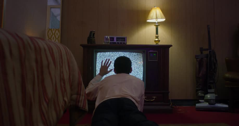 A young teenager is putting his hand on the television