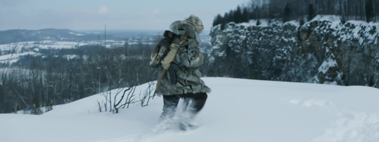 A man wears a heavy animal type coat walking through heavy snow in the wilderness