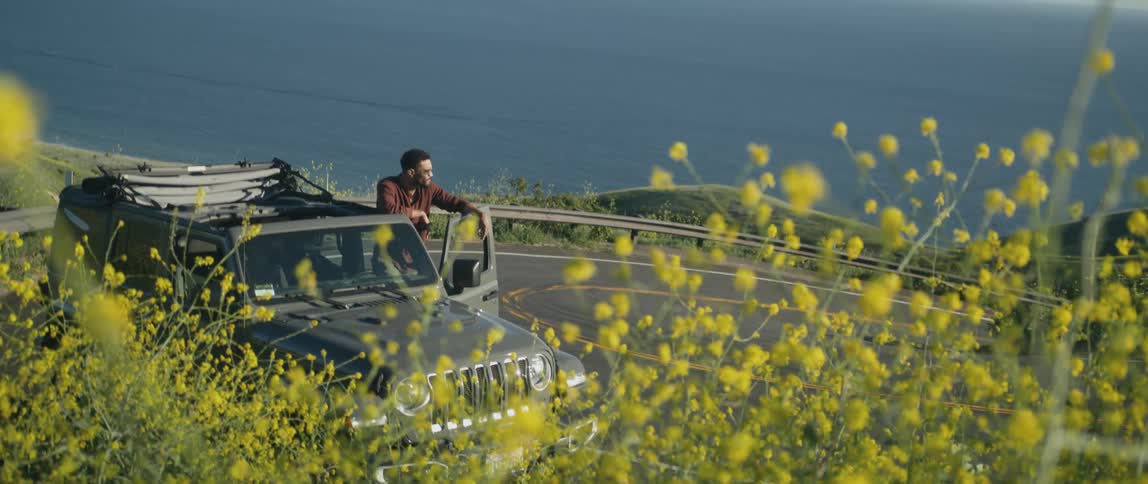 A man is standing outside of his car near the coast