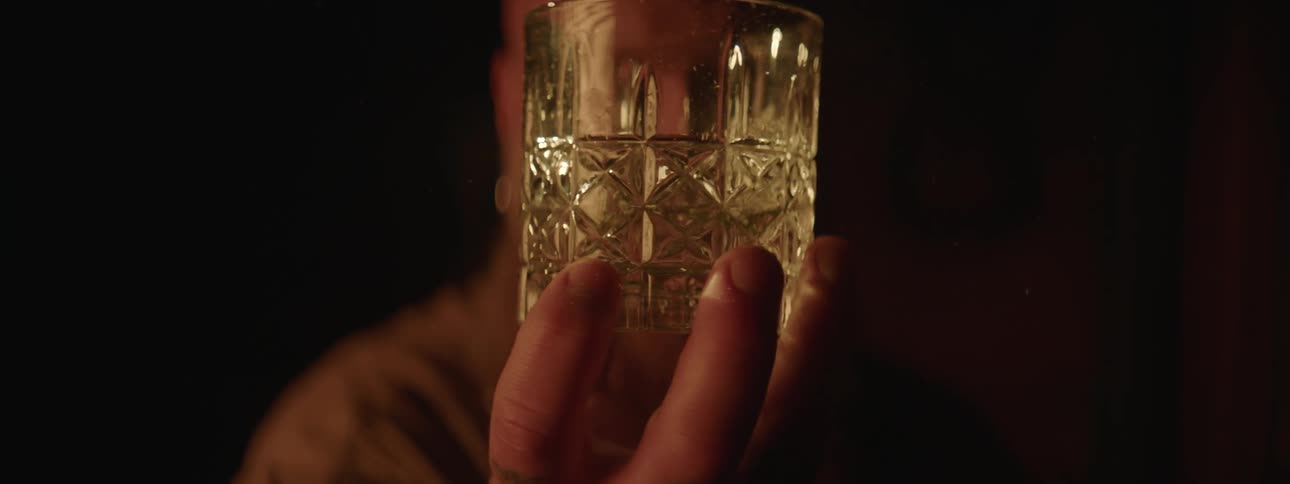 A man is holding a glass with liquid and spinning it with his hand