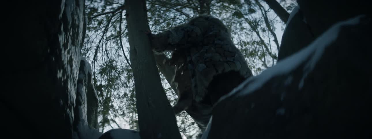 A man swings an ax and throws a bundle of rope while walking through the woods