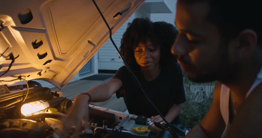 Man and woman are fixing a car together outdoors