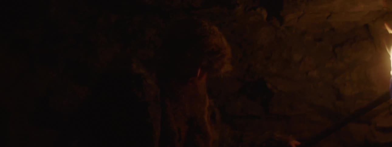 A man uses a torch to navigate the inside of a dark cave