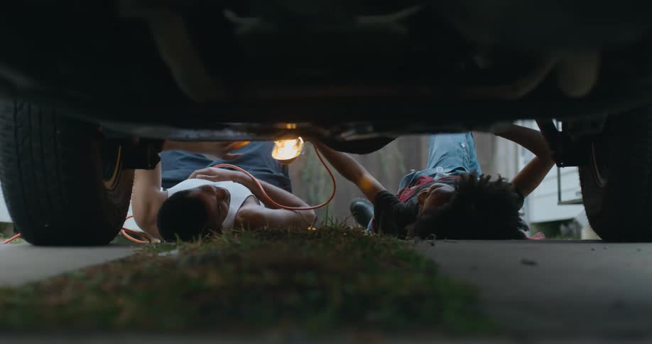 Man and woman are under a car trying to fix it
