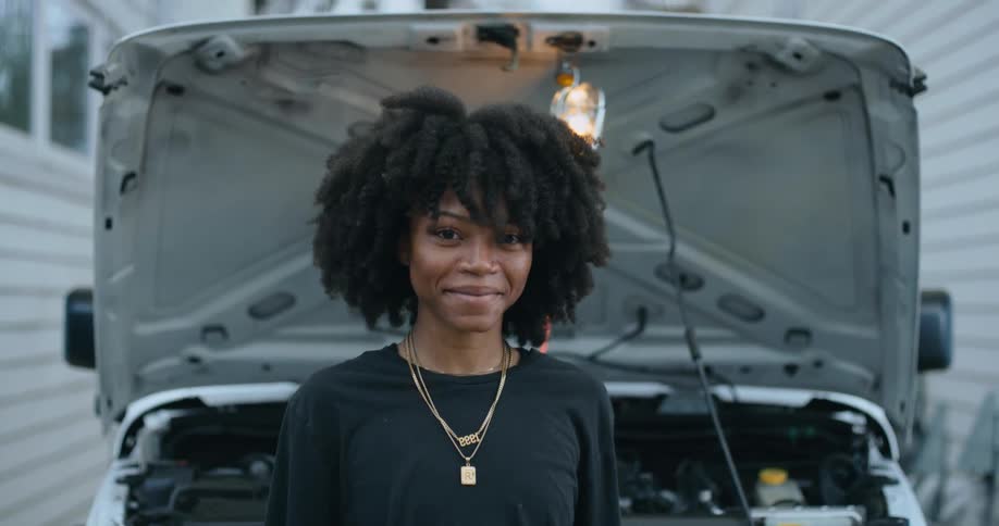 Young happy woman standing in front of the open hood of a car looking at the camera