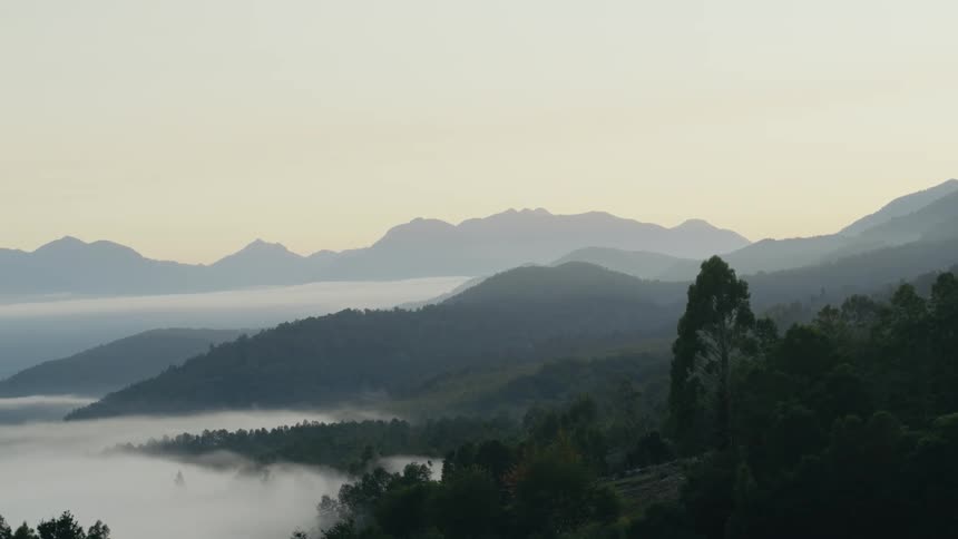 Aerial view of mist rolling at the base of a mountain range at morning