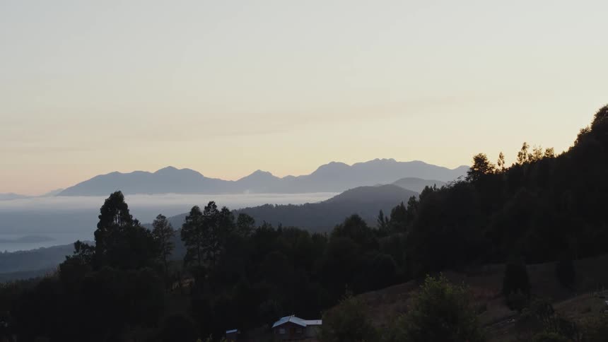 A forest sits on a hill overlooking a beach and mountains