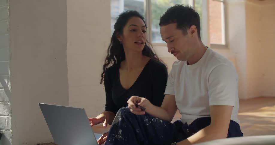 Man and woman are sitting down on the floor next to a laptop