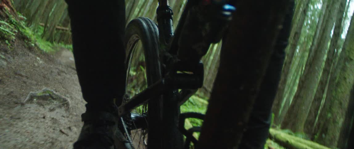 A person riding a bicycle on a trail in the forest goes through a mud puddle