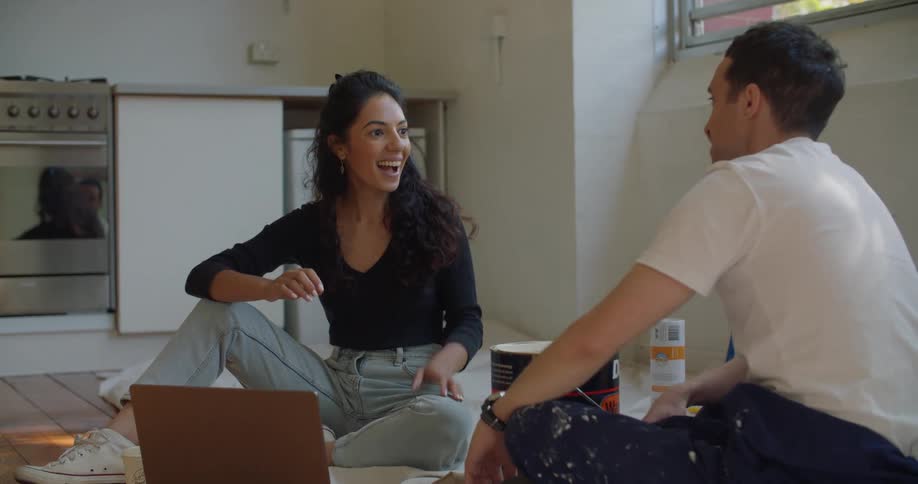 A couple high fives after a woman describes her vision for the apartment while they are both sitting on the floor near the kitchen