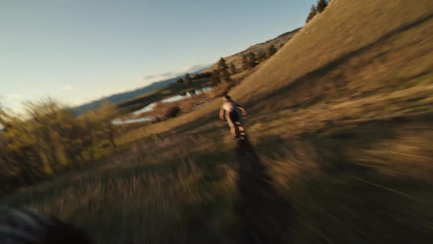 Mountain bike riders descend a grassland single-track trail at sunset