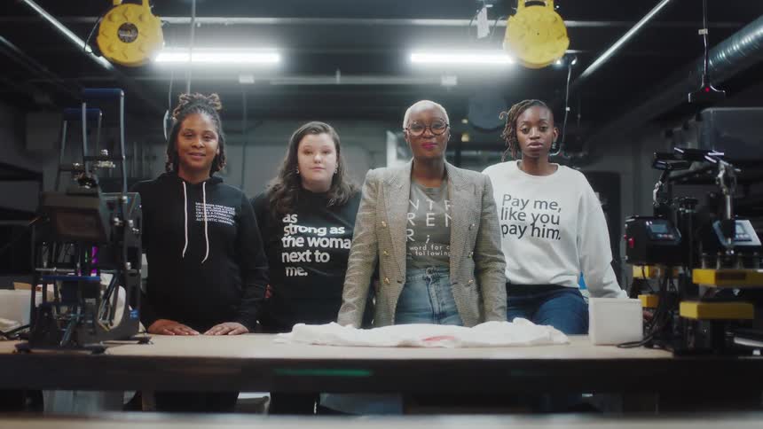 Women working at print shop pose wearing clothes with printed messages