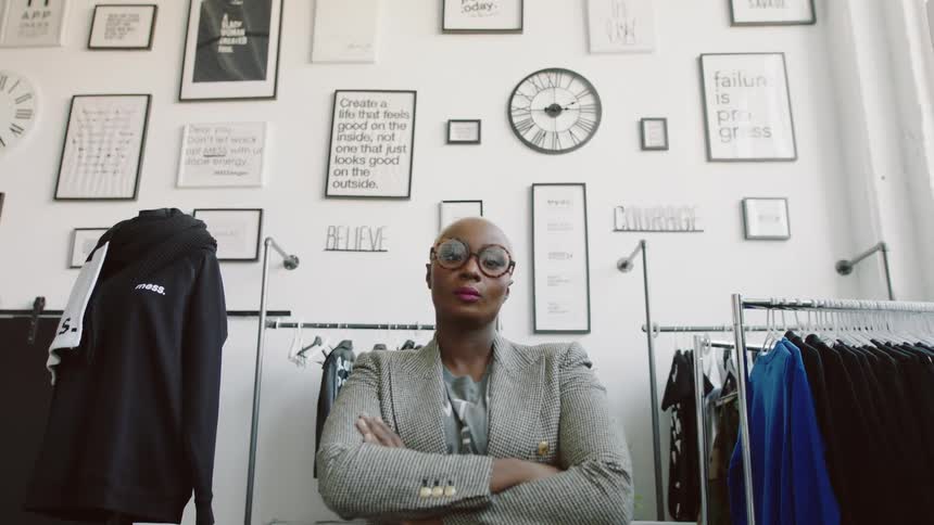 A woman looks angry as she sits in a room with clothes racks