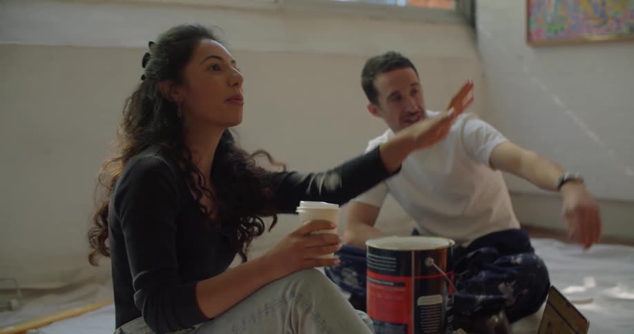 A man and woman take a break from painting to look at a laptop
