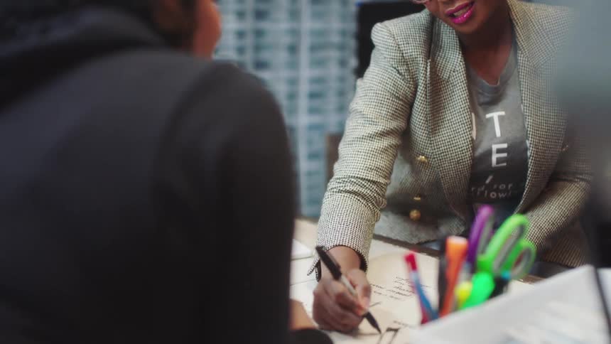 A female employee instructs a client what to do on a piece of paper on the desk in between them