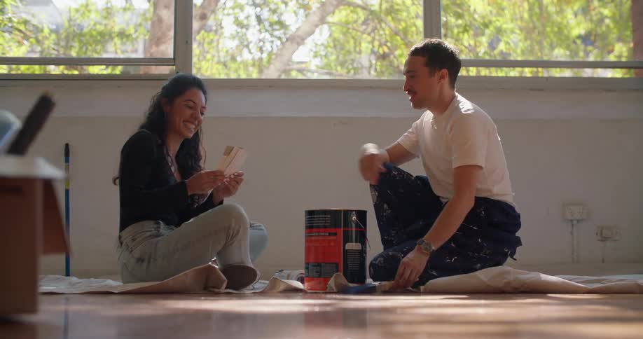 Man and woman laugh while discussing strips of paint samples near large paint can