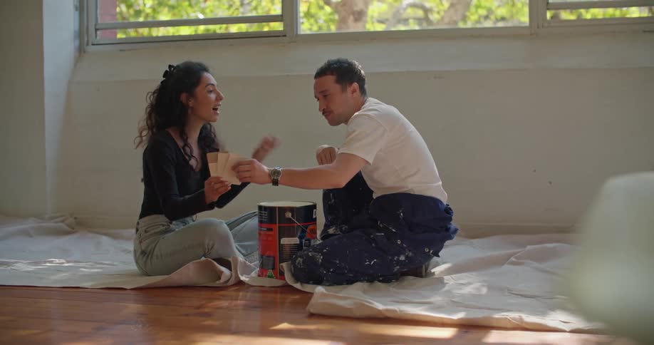 Man and woman are sitting down on the floor next to the paint