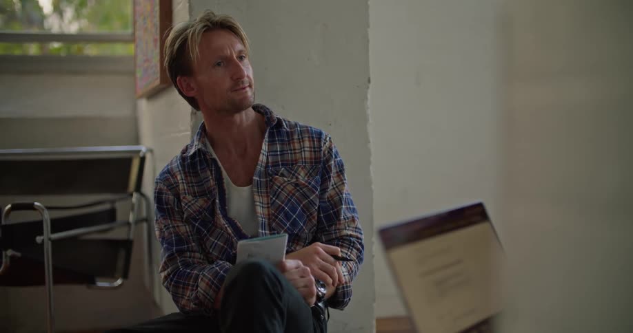 Man sitting in a room listens to someone and takes notes with pen and paper