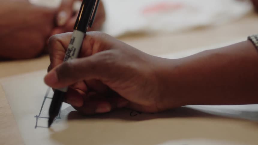 A person uses a marker to draw a fashion design on a sheet of paper